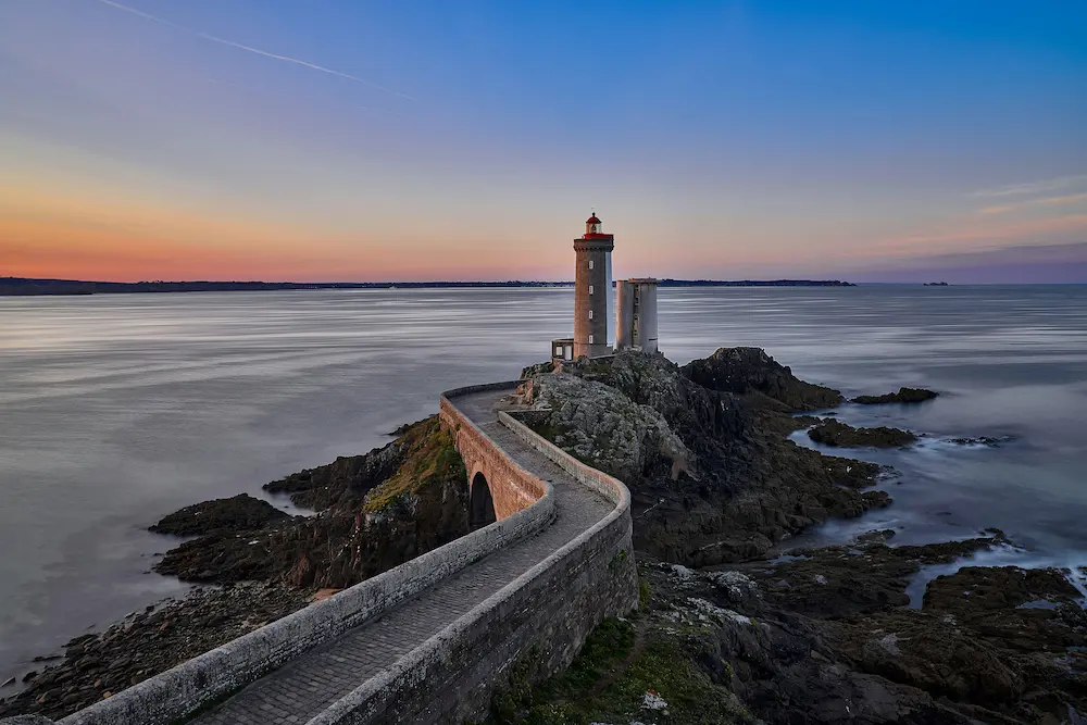 Coastal lighthouse and rocky shoreline at sunset on the Brittany Atlantic coast, France digital detox retreat destination