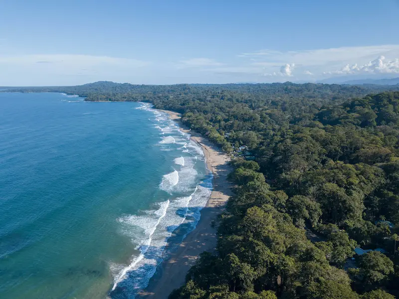 Aerial view of turquoise Caribbean Sea, white sand beach and dense jungle on Costa Rica coast, digital detox retreat destination